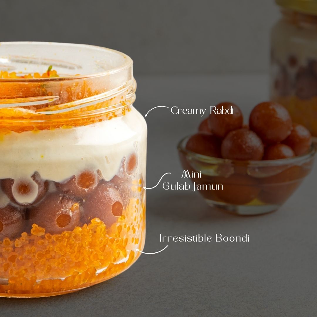 Jar with arrows pointing to layers: boondi at the bottom, mini gulab jamuns in the middle, and rabdi on top, highlighting each dessert component.
