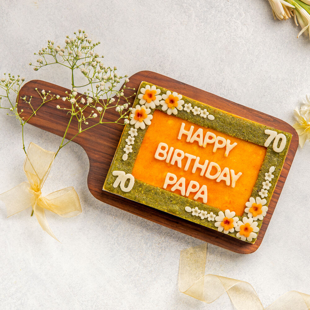 A rectangular mithai cake made from badam and pista with intricate floral patterns and "Happy Birthday Papa" written in the center, perfect for a festive occassion