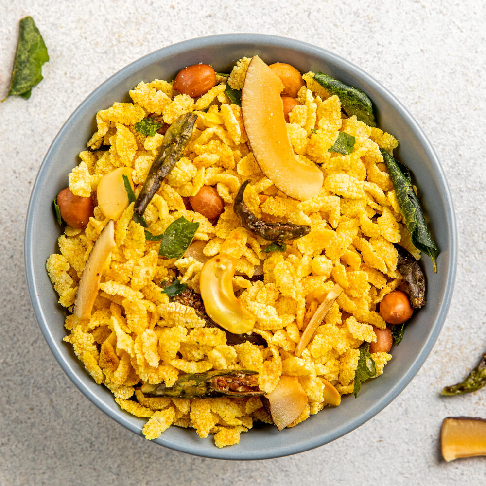 A bowl of crunchy chiwda mixture featuring a blend of flattened rice, peanuts and dry fruits, garnished with spices and curry leaves for a savory flavorful snack