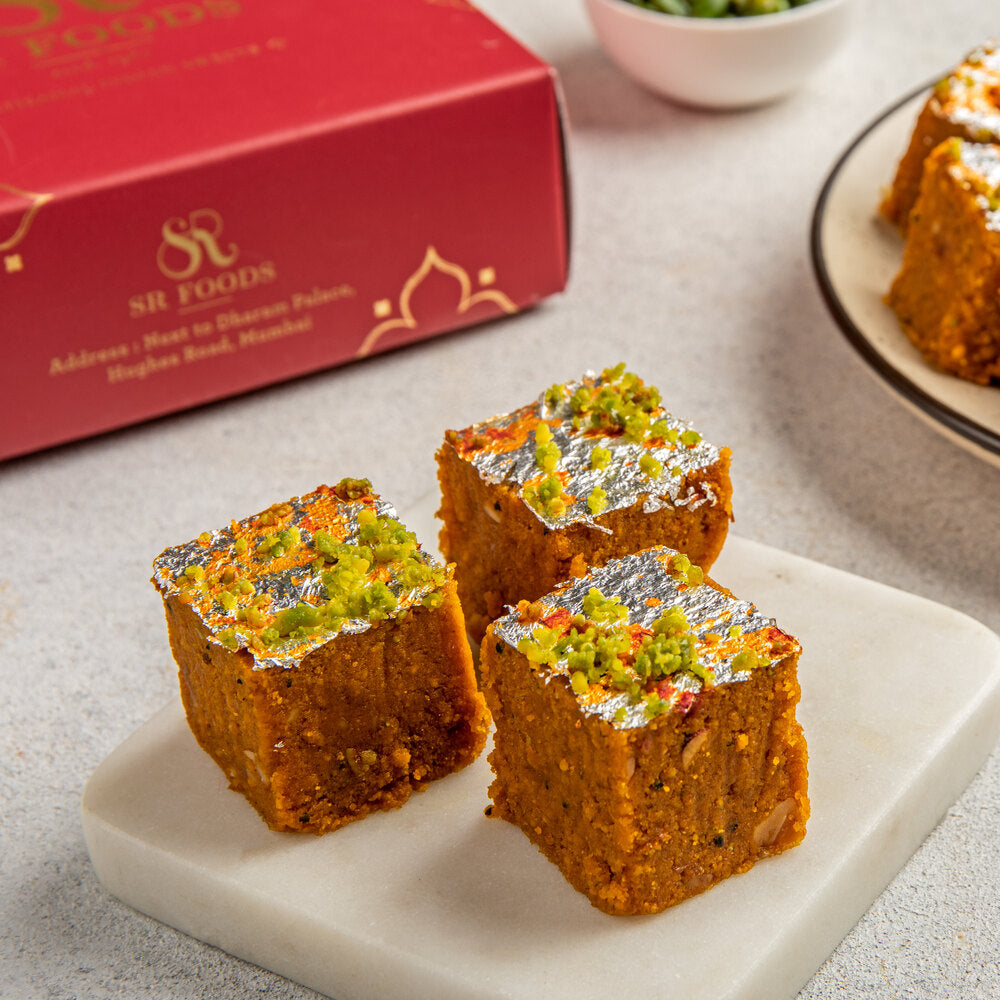 3 beautifully crafted besan barfis siting on a plate adorned with silver varak and pistachio