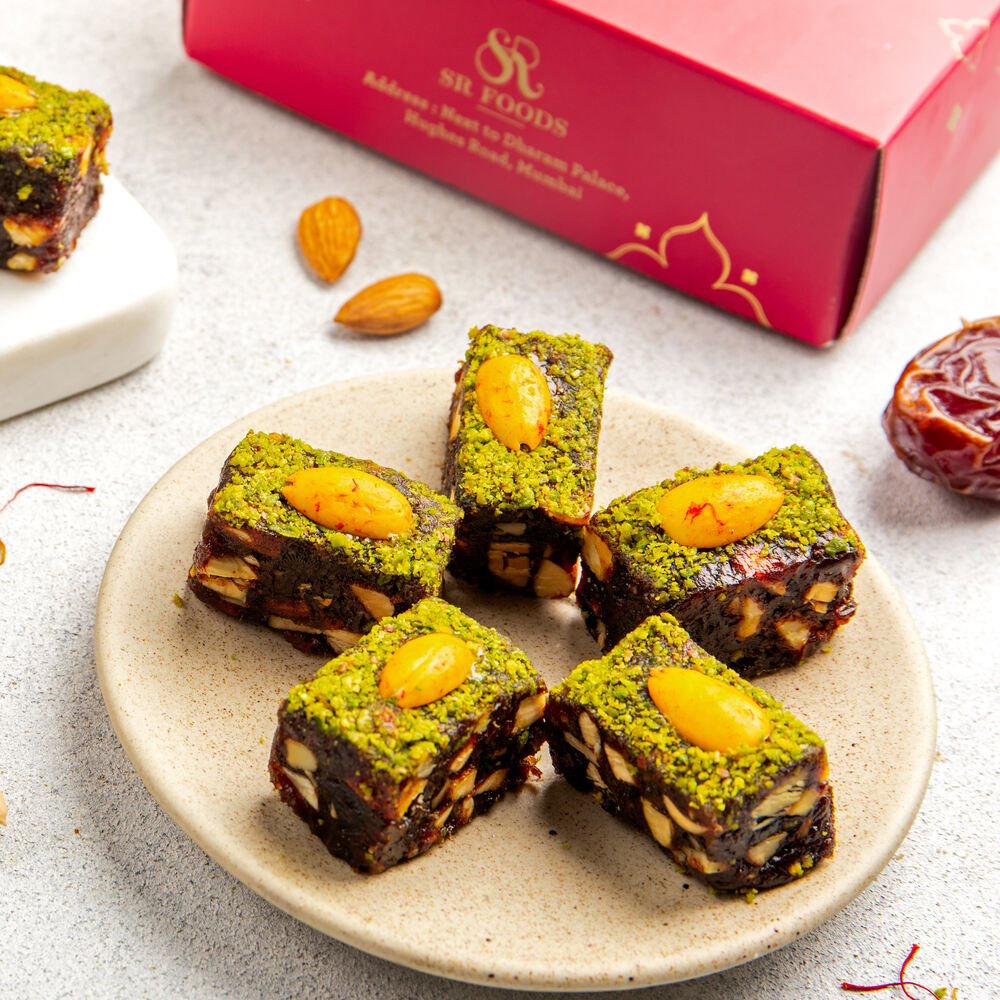 Beautifully crafted khajur badam barfi pieces, each decorated with fresh pistachio powder and an almond piece.