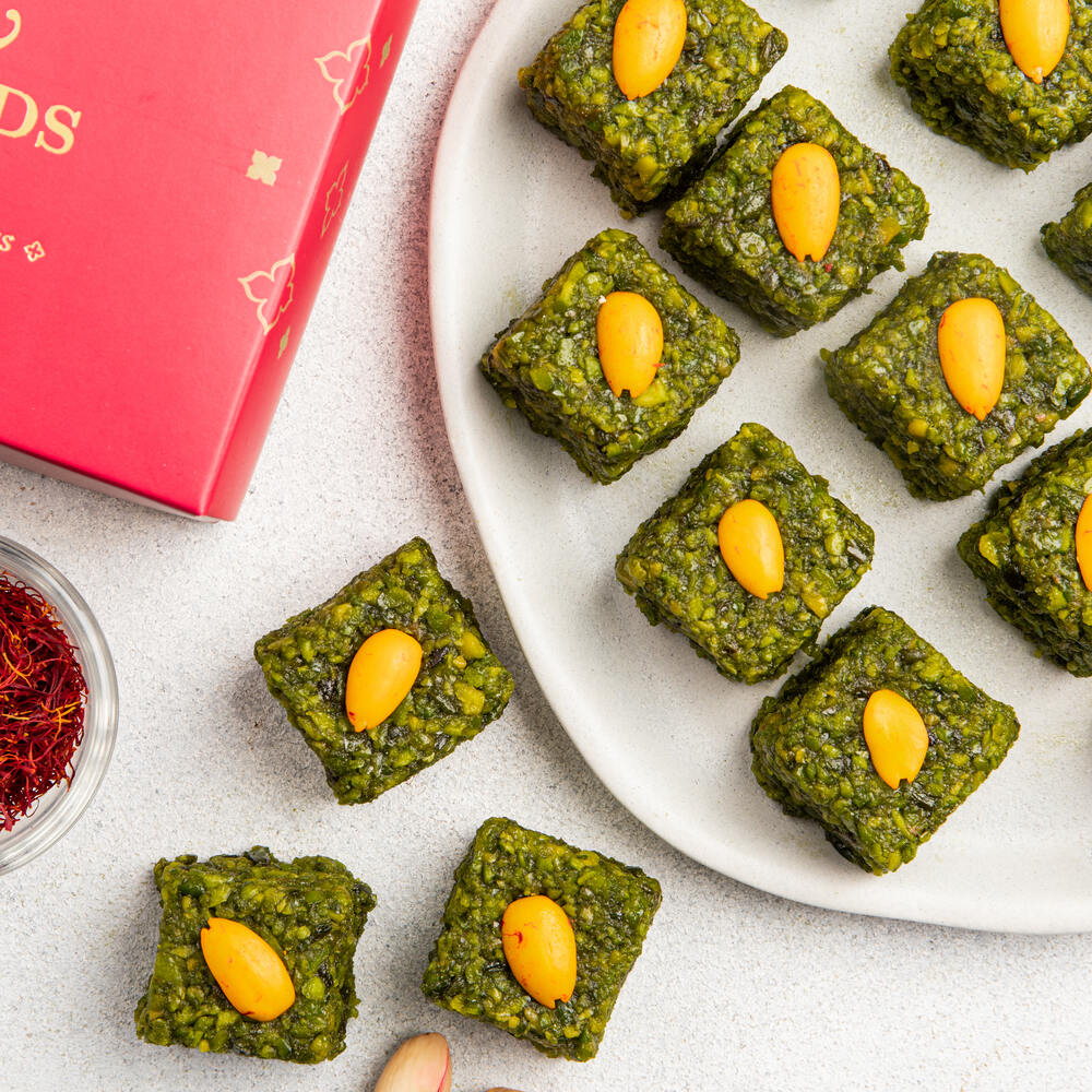Beautifully crafted pishori pista barfis with visible pistachio pieces and adorned with almond decoration. 