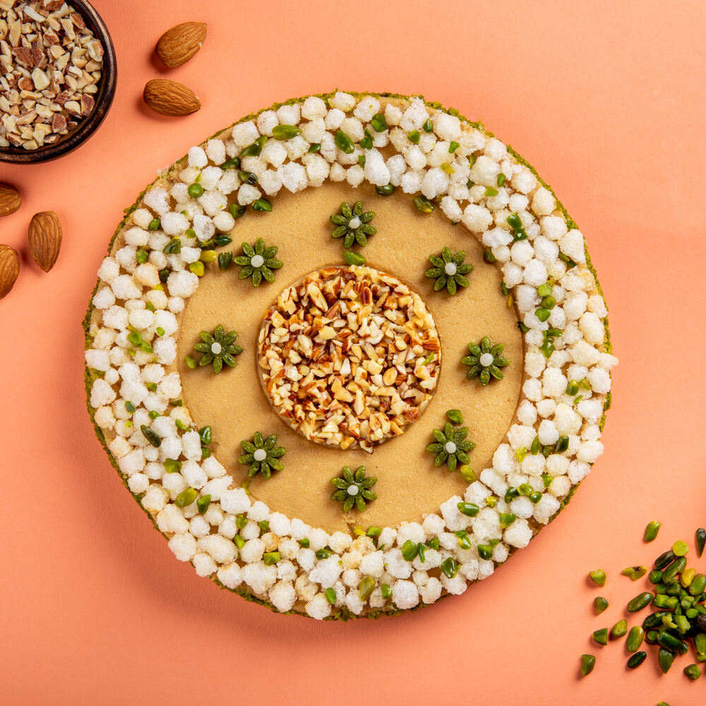 Circular mithai cake made of nolen gud with a beautiful floral decoration on top consisting of almonds, pistachios and crunchy gond