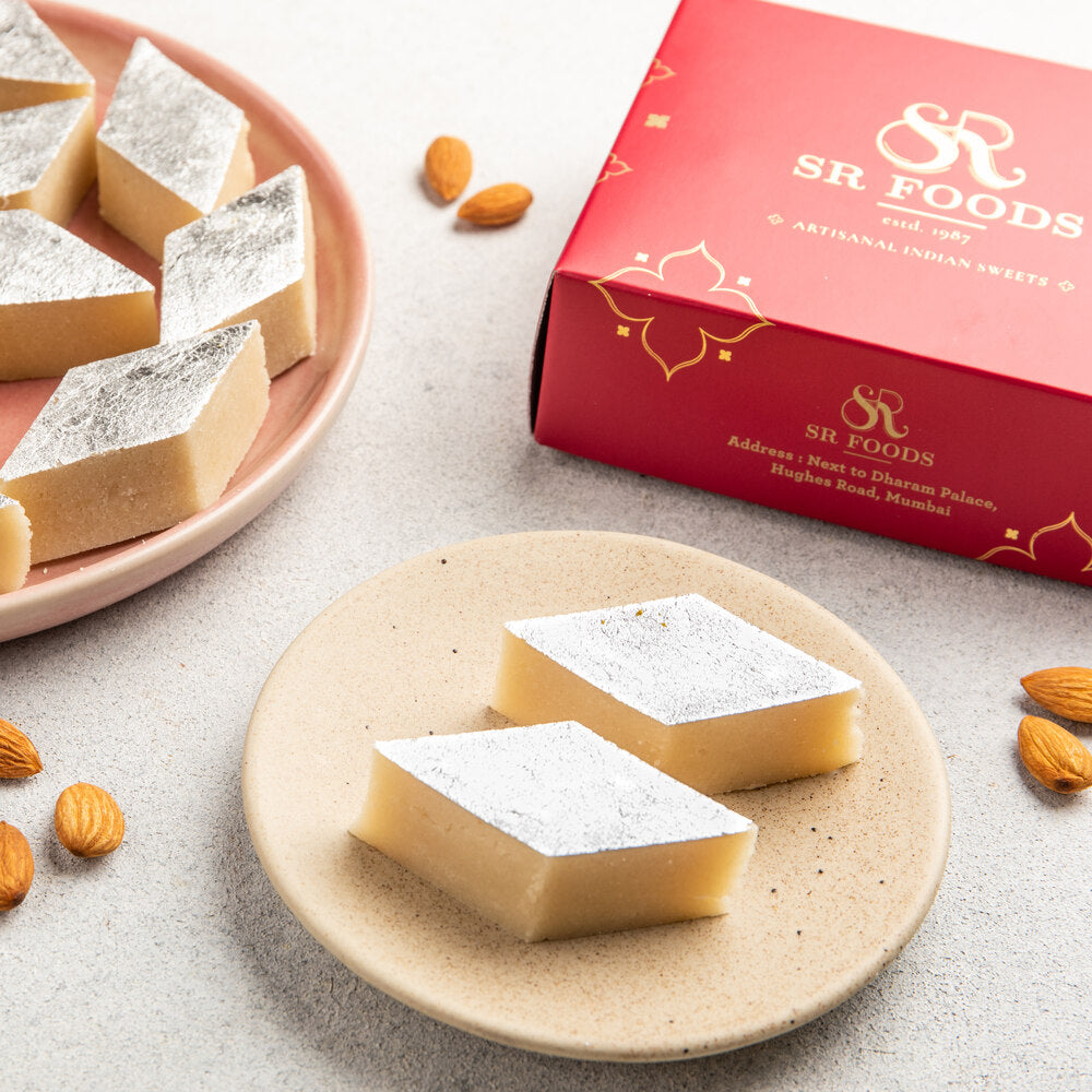 Beautifully crafted sugar free mamra badam barfi pieces cut into diamond shape pieces and adorned with silver varak
